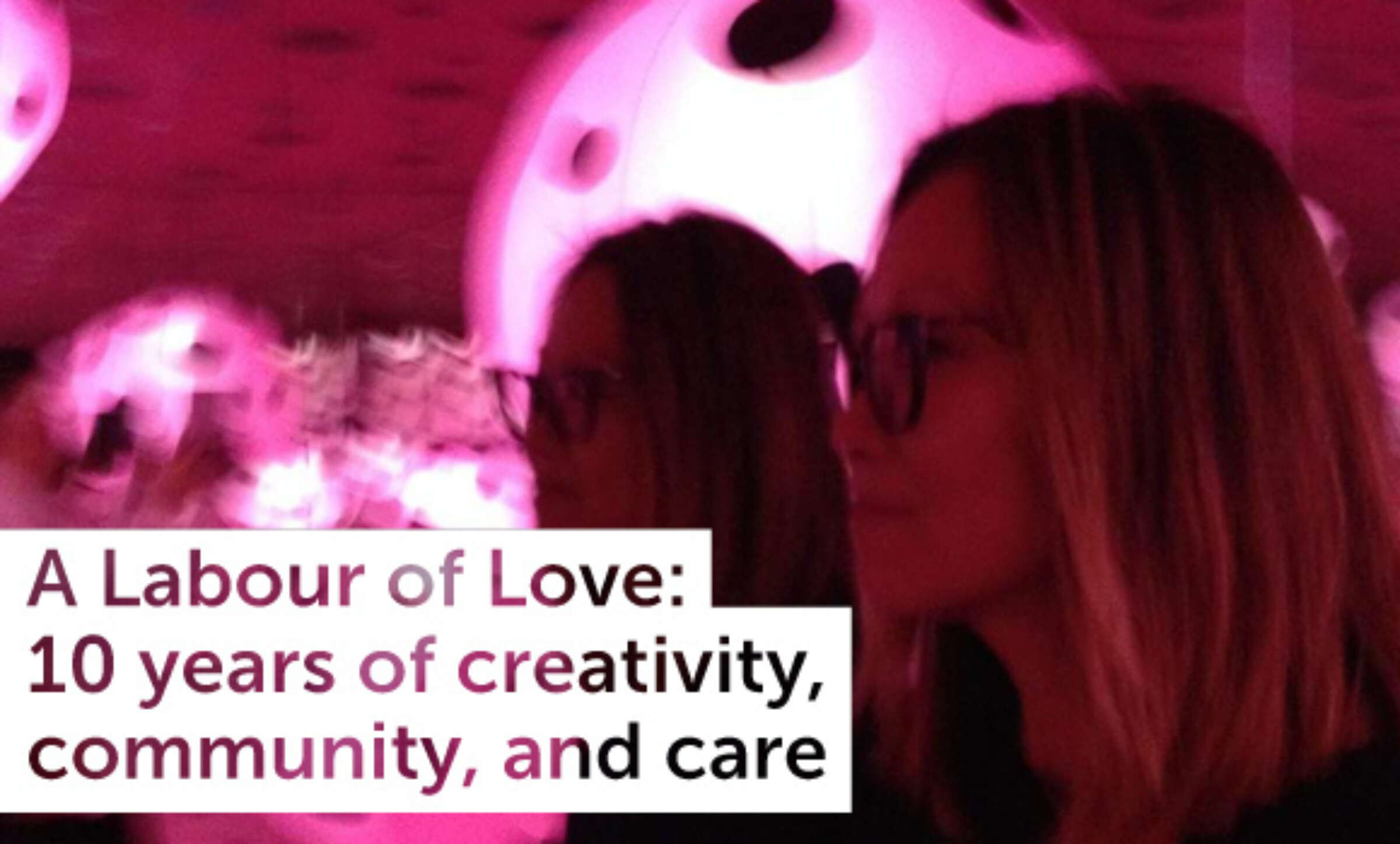 A person with shoulder-length hair and glasses is looking ahead in a pink-lit environment. Text overlay reads: "A Labour of Love: 10 years of creativity, community, and care.
