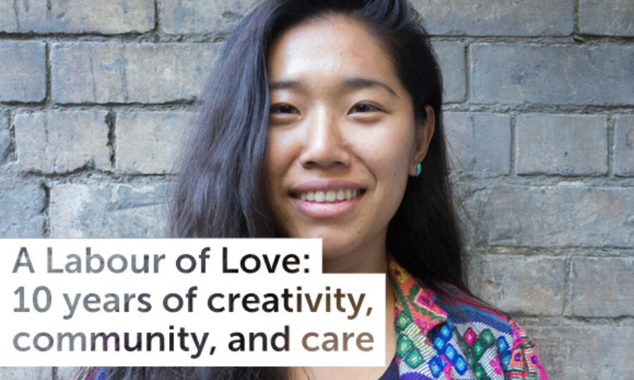 A young person with long dark hair is smiling in front of a textured brick wall. Text overlaid on the image reads, "A Labour of Love: 10 years of creativity, community, and care." They are wearing a colorful patterned jacket.