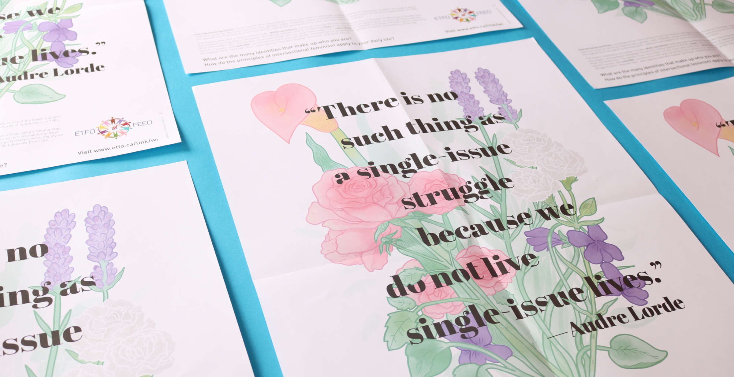 Several posters with floral illustrations and a quote from Audre Lorde, "There is no such thing as a single-issue struggle because we do not live single-issue lives," are laid out on a blue surface. The posters feature pink, purple, and green flowers.