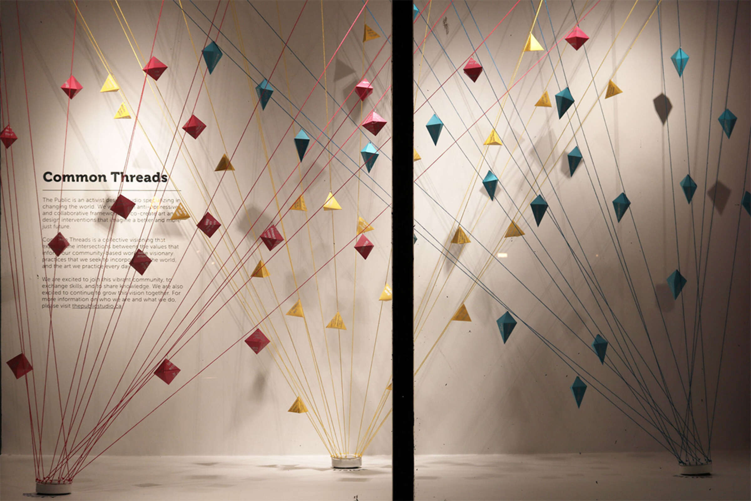 A display window features a geometric art installation titled "Common Threads" with interconnected multicolored threads forming diamond-shaped patterns. The text describes the artwork's theme, emphasizing connection and interaction. The setting appears well-lit.