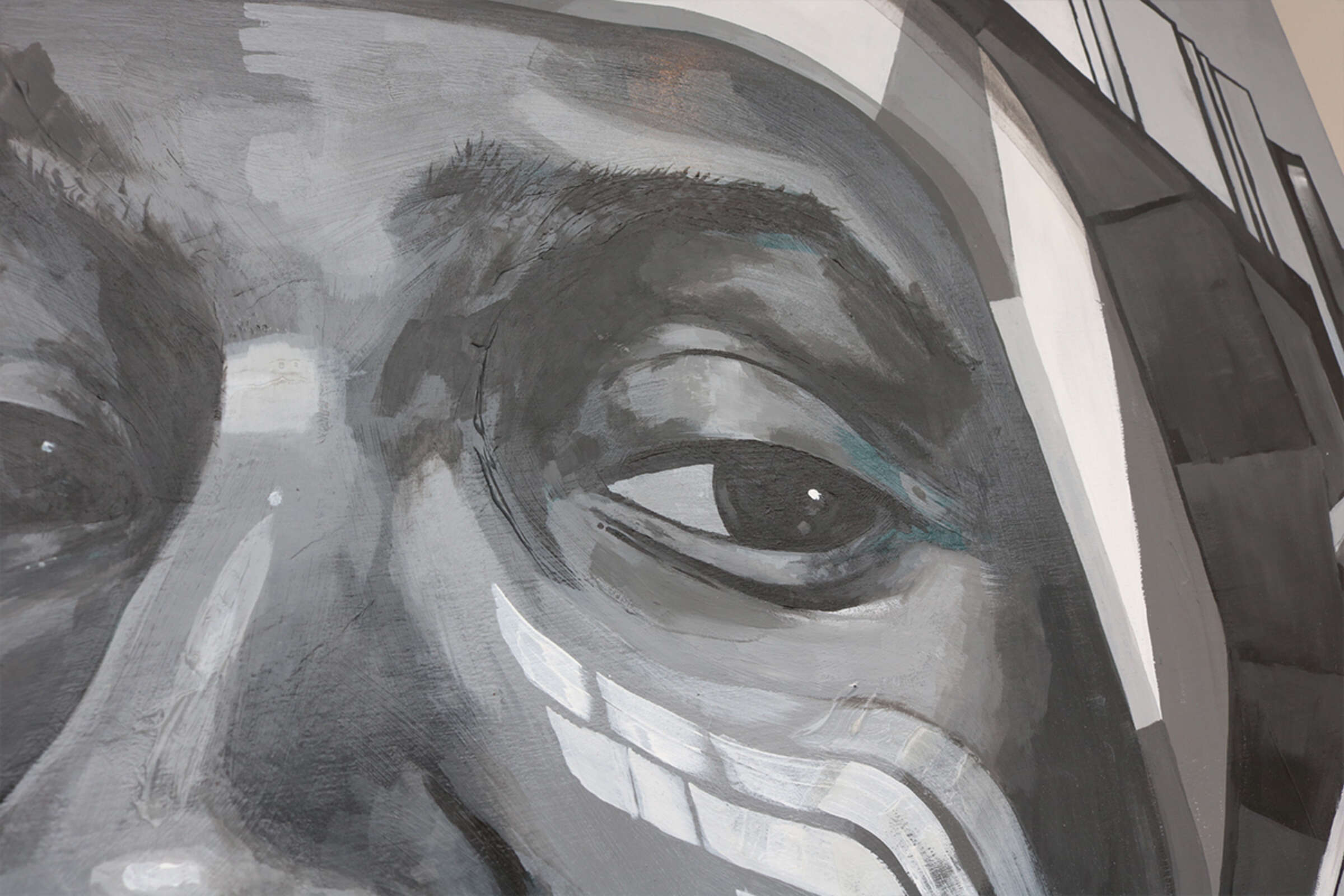 Close-up of a monochromatic mural depicting a person's face. Only one eye and part of the nose are visible, with intricate patterns and shapes painted around the eye area. The artwork uses varying shades of gray to create depth and texture.