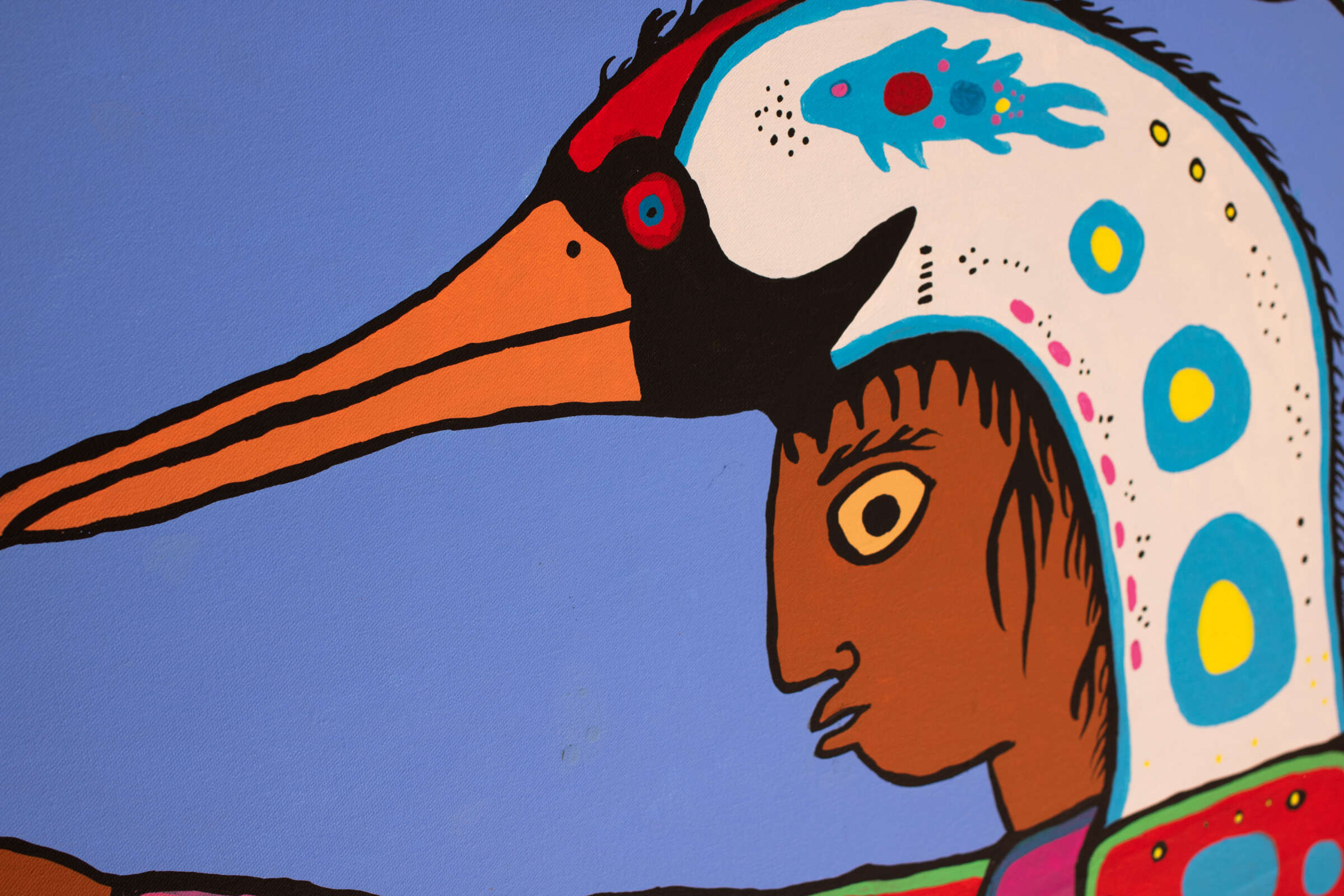 A vibrant mural depicts a person with dark skin and stylized features wearing a colorful bird headdress. The bird's long orange beak extends outwards, and the headdress is adorned with multi-colored patterns, set against a light blue background.