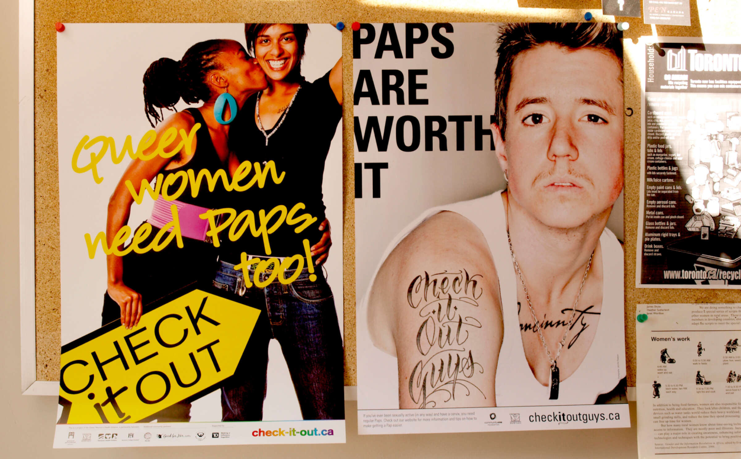 Two posters on a bulletin board. The left features two people embracing with the text "Queer women need Paps too! Check it out." The right shows a person with tattoos, with the text "Paps are worth it." Both posters promote checkitout.ca.