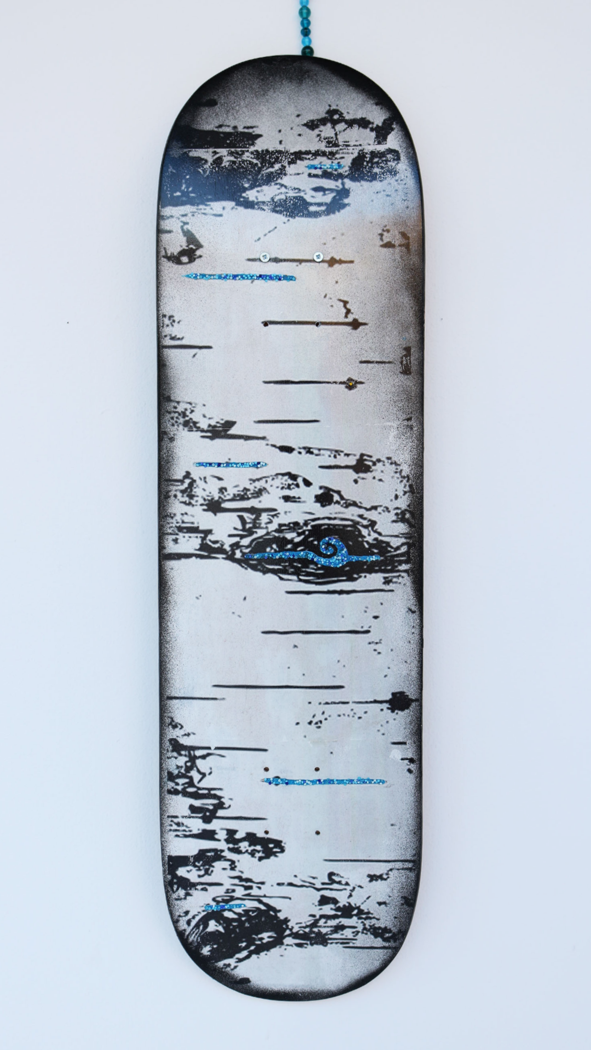 A skateboard deck with an abstract design featuring black, white, and blue colors, giving it a distressed, grungy appearance. The design appears to have scratch-like and paint-splatter elements across the entire deck.