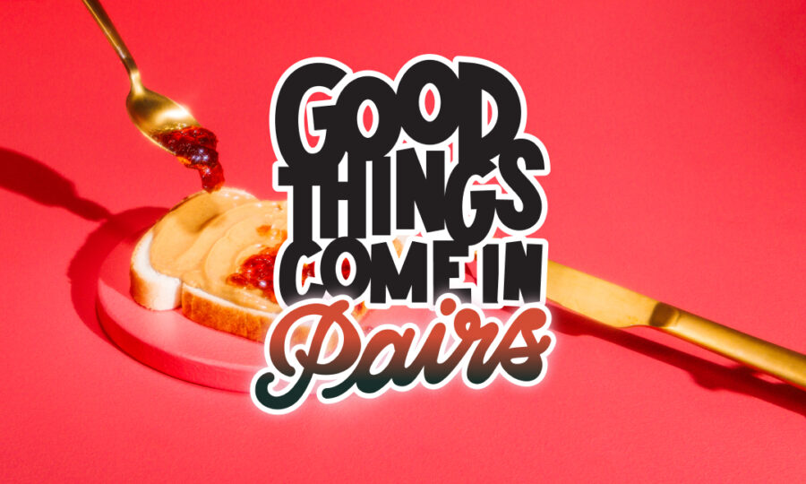 A spoon with jam spreads onto a slice of bread with a knife nearby, set against a vibrant red background. Overlaid text says, "Good things come in pairs.