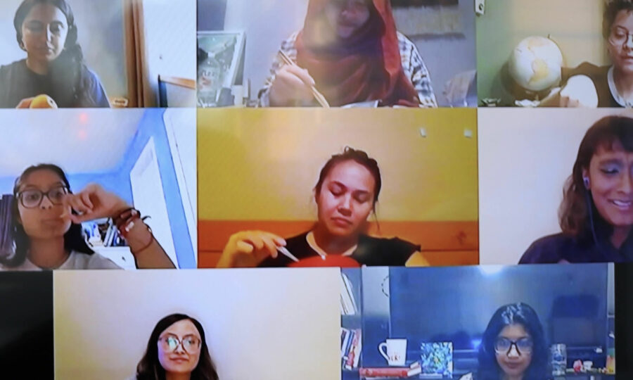 A screenshot of a video call shows nine women in separate boxes, each engaged in different activities. Some are eating, one is holding a globe, and another is writing. They appear to be in a meeting or casual group conversation.